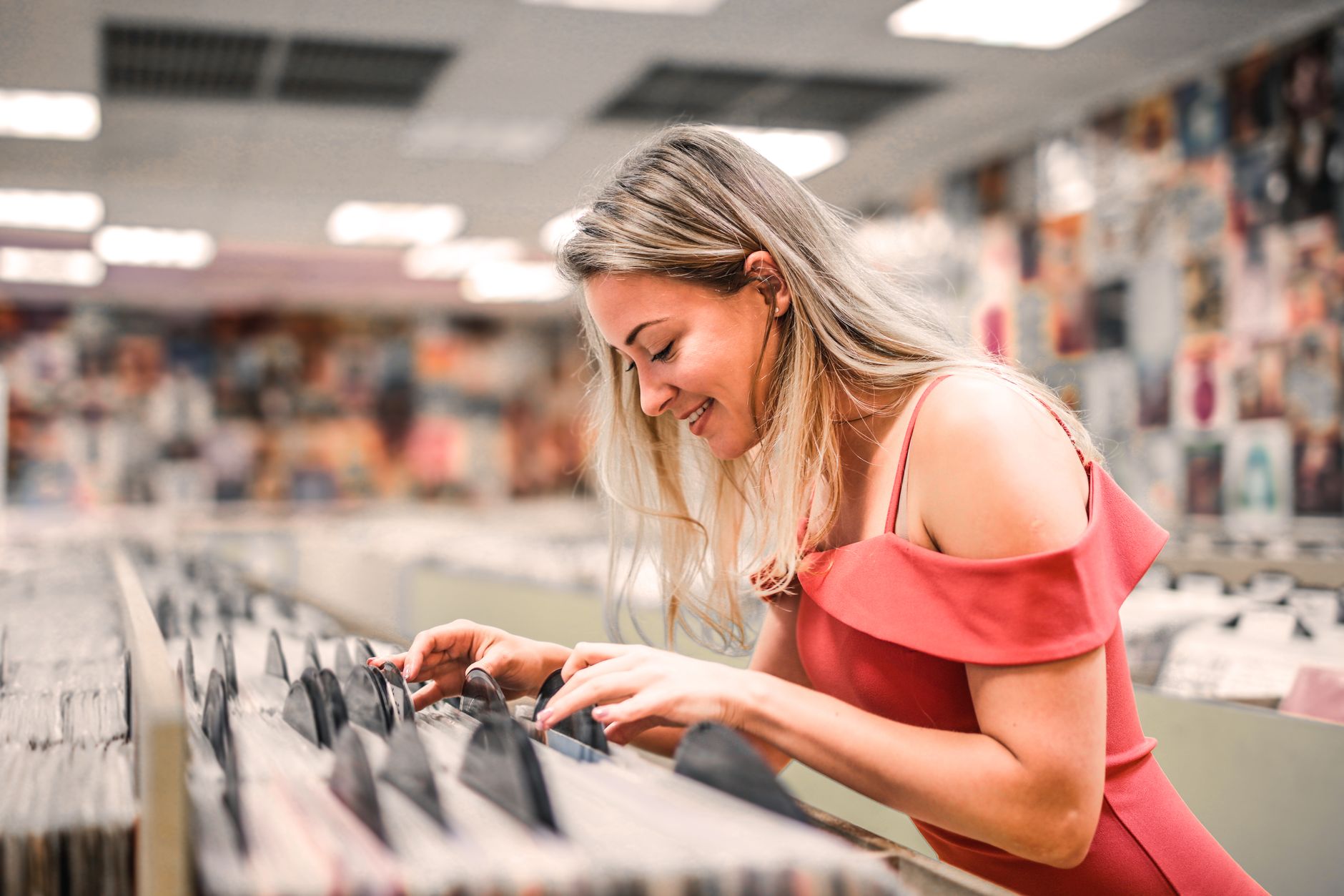 Woman in pink dress enjoying browsing vinyl records at a music store.