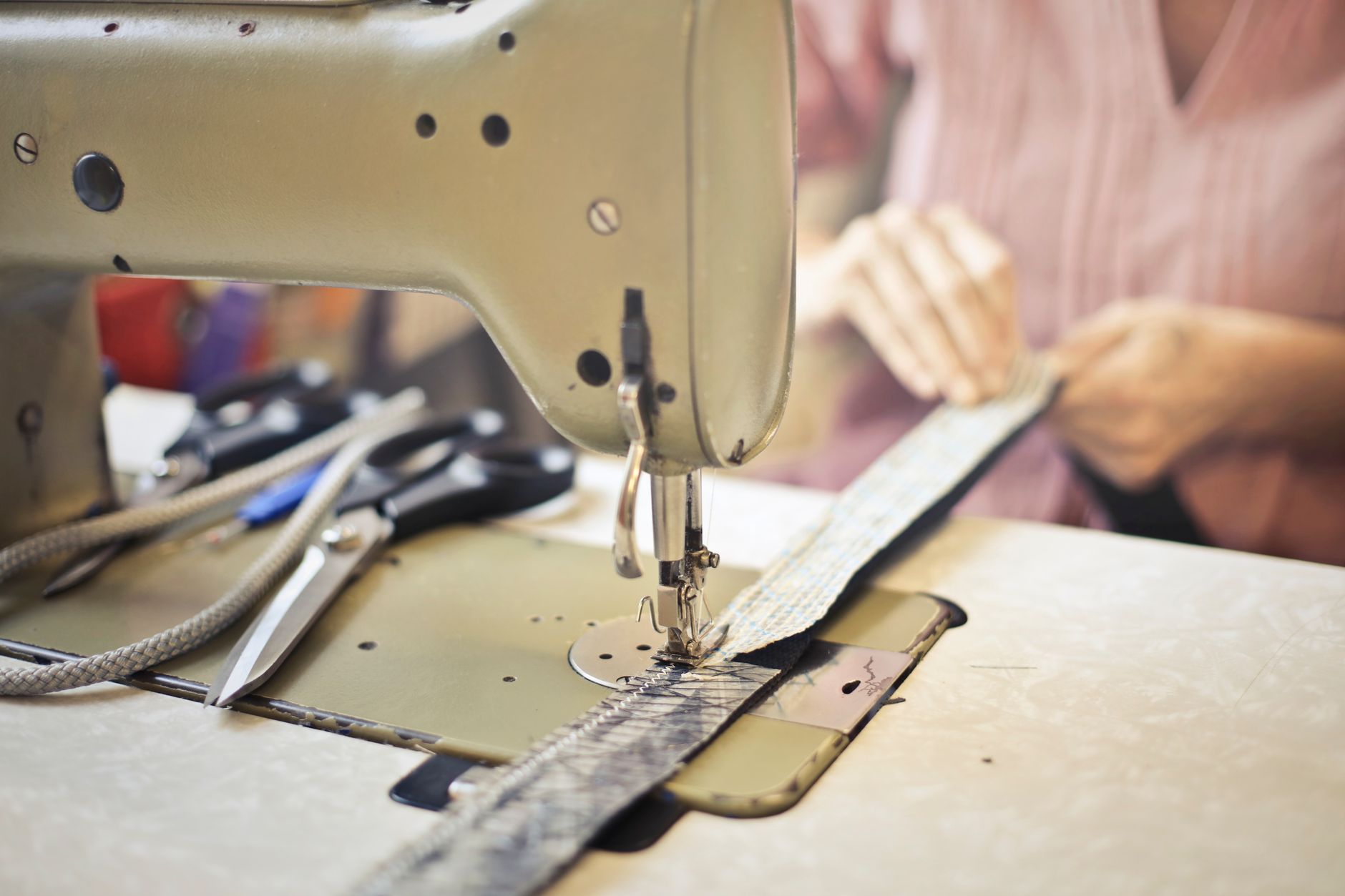 Crop craftswoman in casual wear sitting at old fashioned sewing machine and stitching pieces of fabric while working in workshop