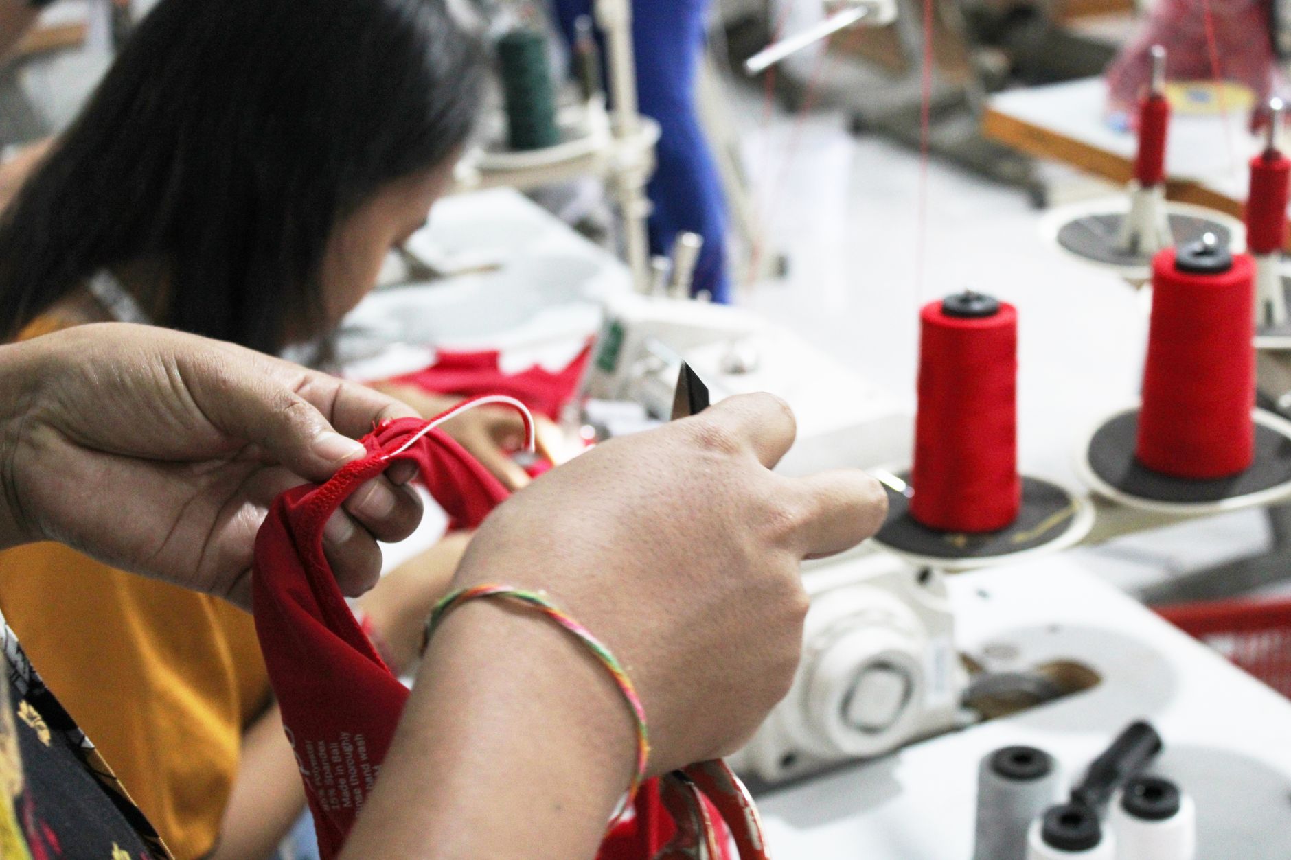 Close-up of hands working with fabric in a sewing workshop, surrounded by spools and machinery.