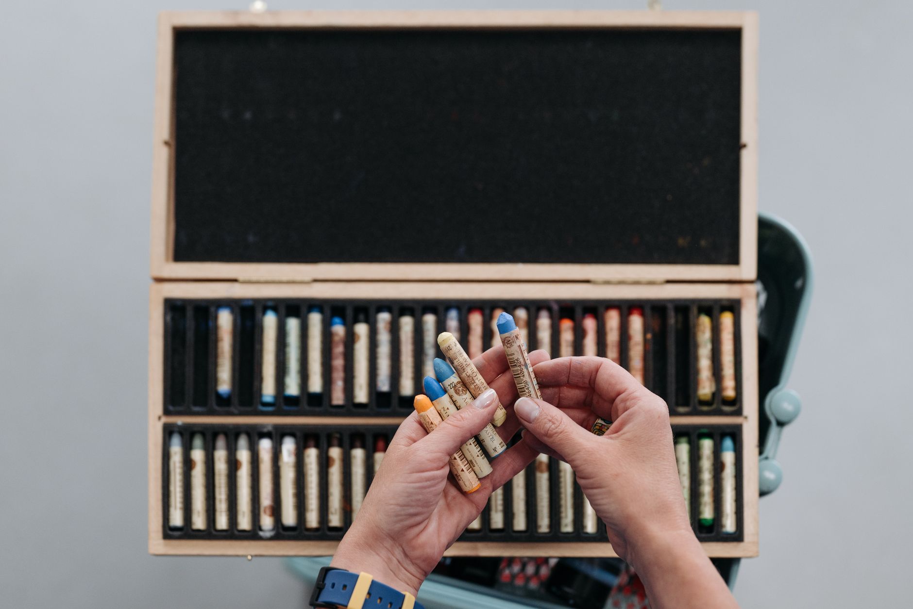 Hands selecting vibrant oil pastels from a wooden art case. Perfect for creative projects and art inspiration.