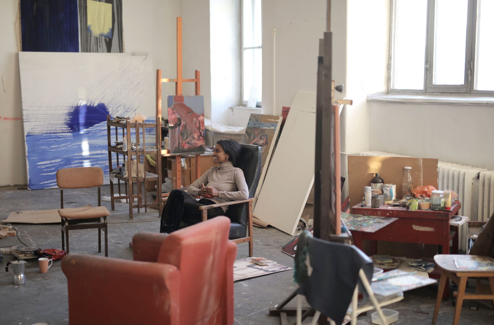 A creative and cozy art studio with a relaxed artist sitting amidst paintings and art supplies.