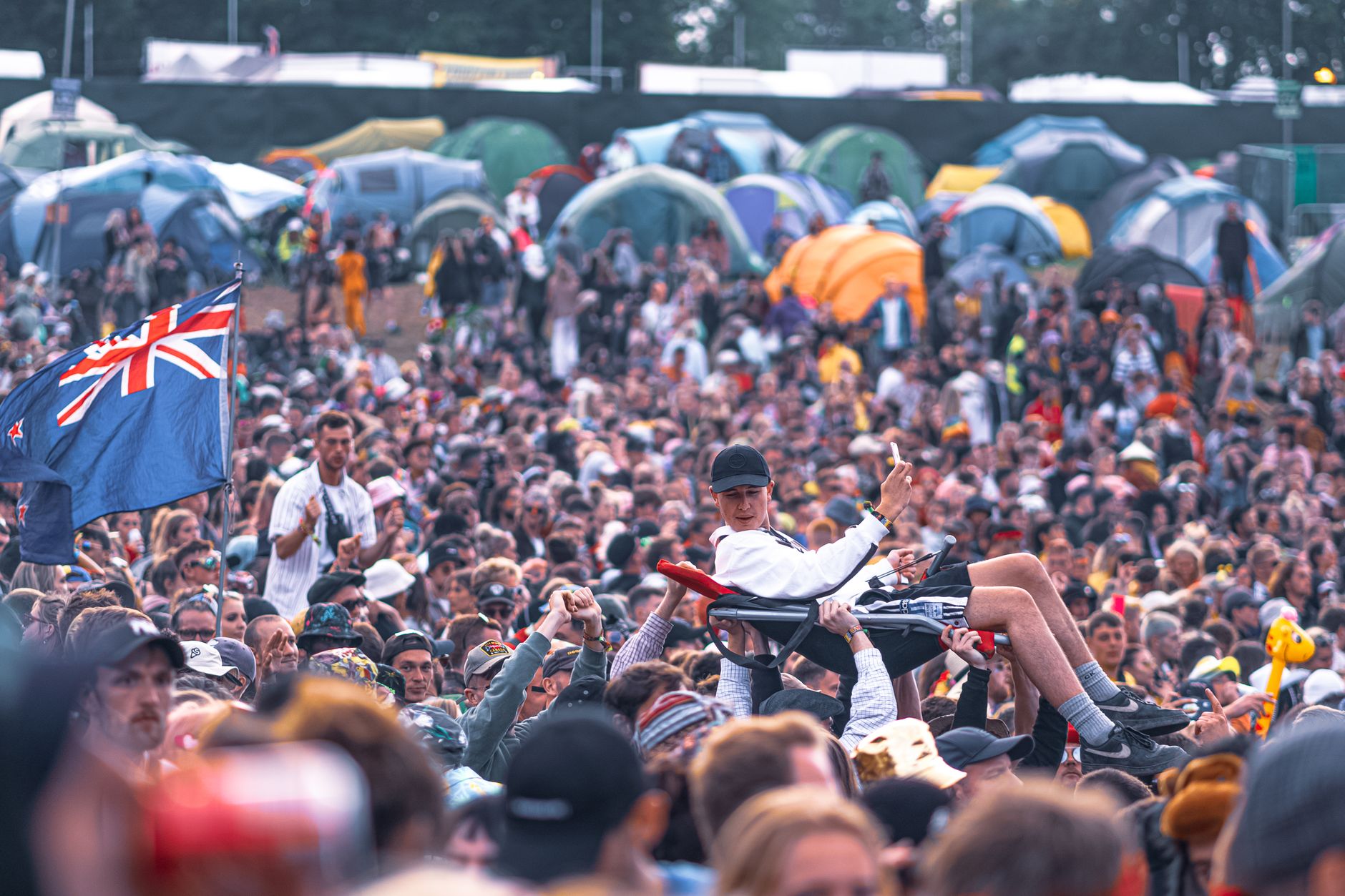 Exciting scene of a crowd surfing at an outdoor music festival with camping tents.