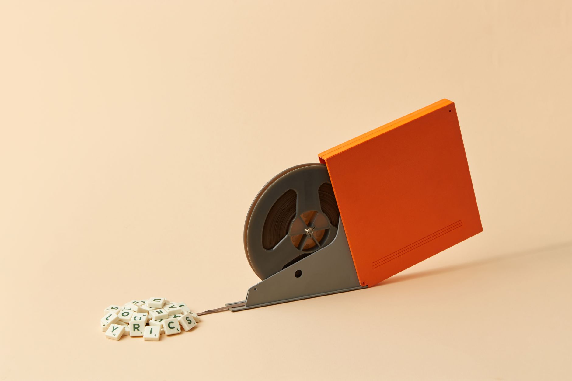 Bobine de film grise dans un boîtier orange, avec une pellicule menant à un tas de tuiles de lettres blanches sur fond beige.