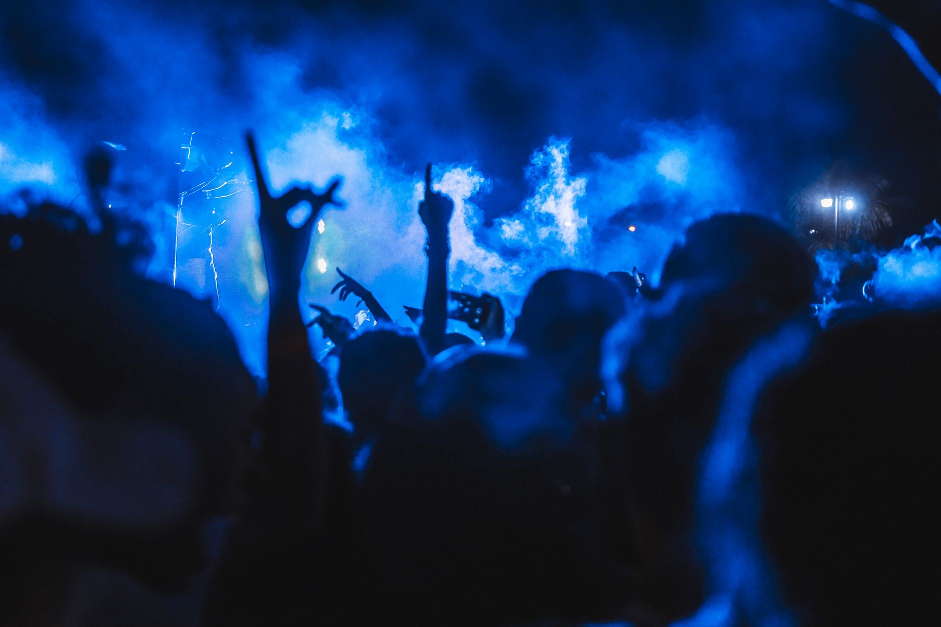 Foule en silhouette de nuit, bras levés devant une fumée éclairée en bleu, lors d’un concert.