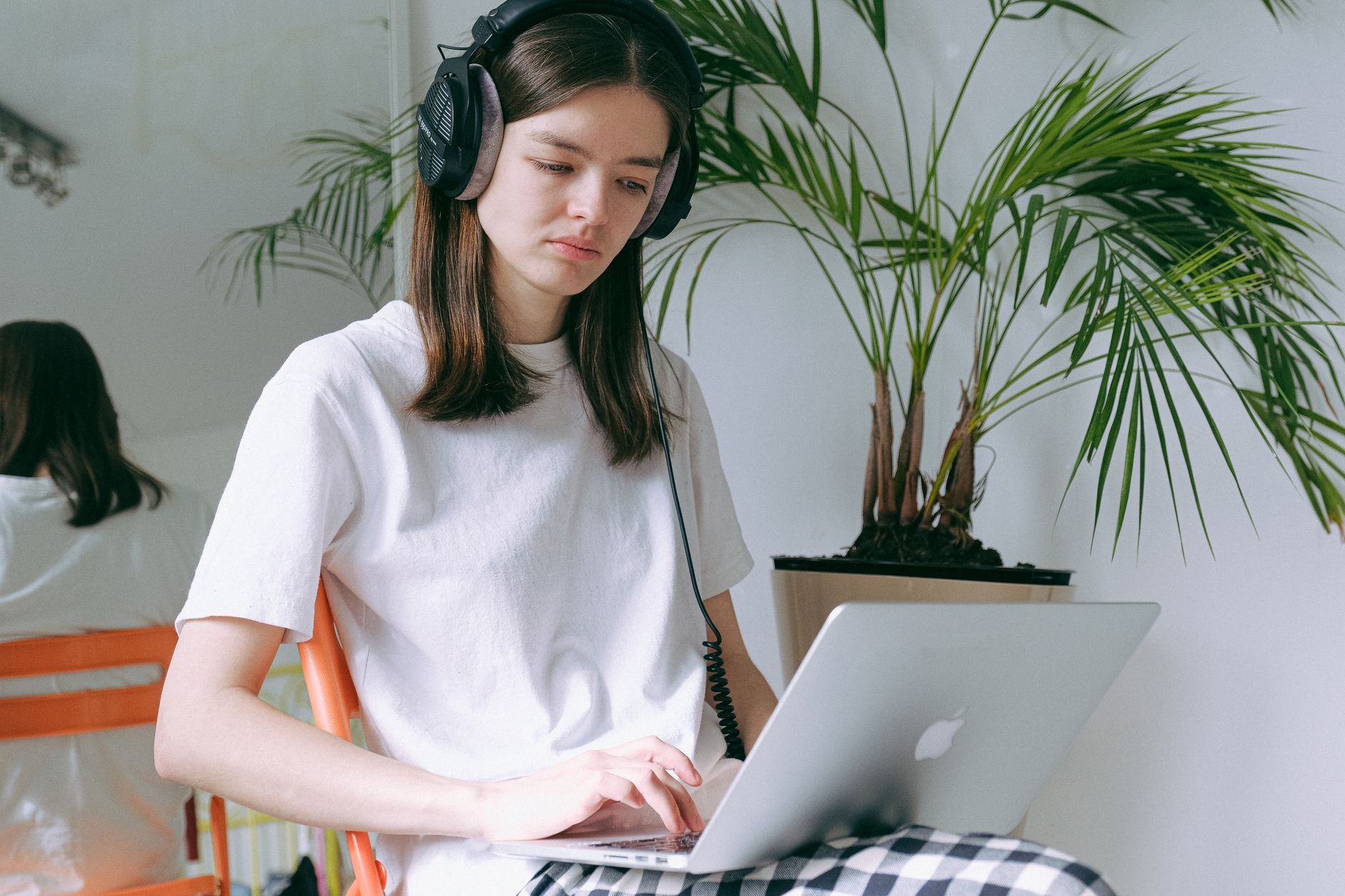 Jeune femme avec un casque audio travaillant sur un ordinateur portable, assise près d’un palmier en pot dans une pièce claire.