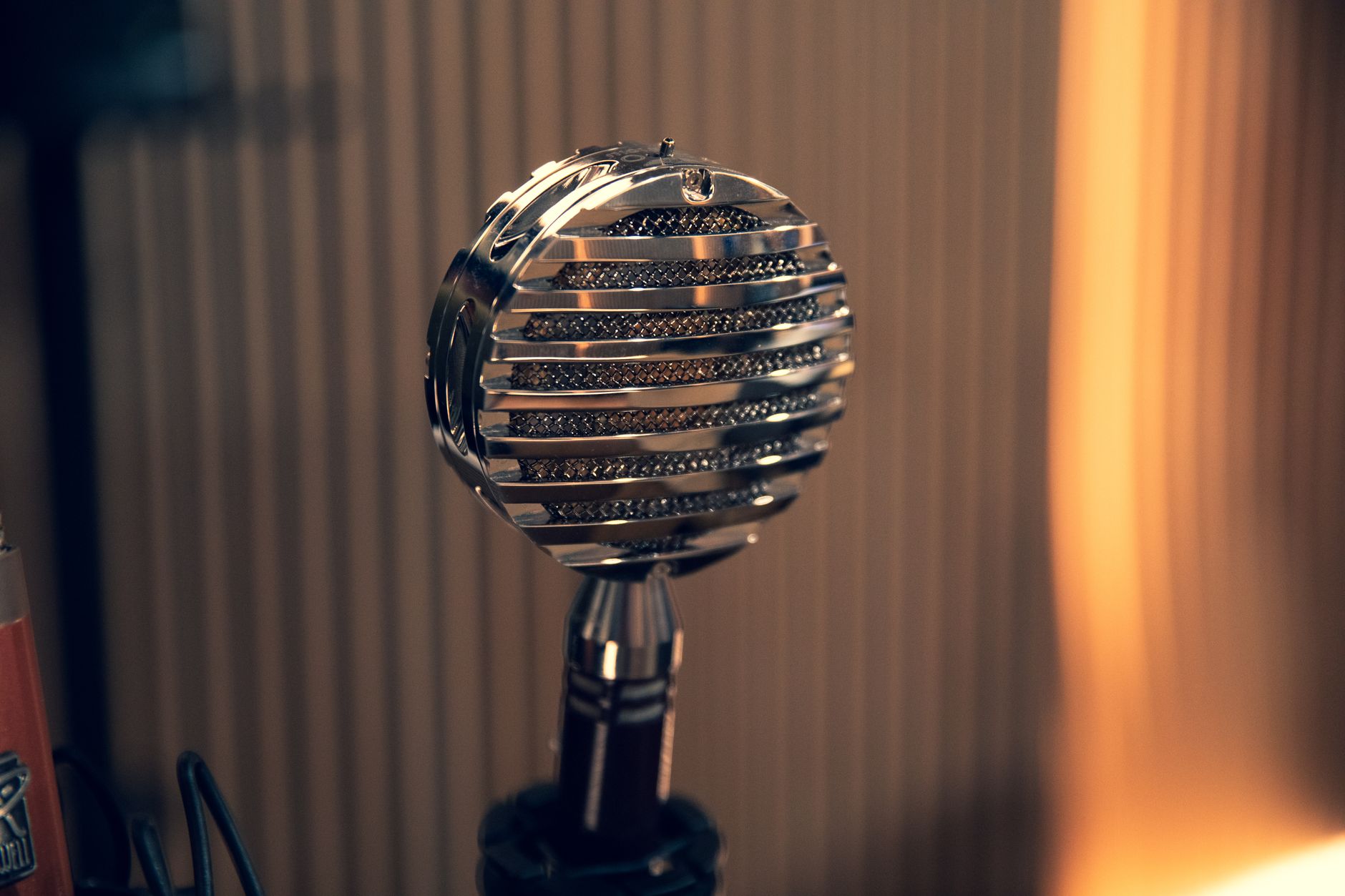 Microphone rétro chromé à grille à lamelles horizontales, sur un pied, devant des panneaux verticaux éclairés d’une lumière chaude.